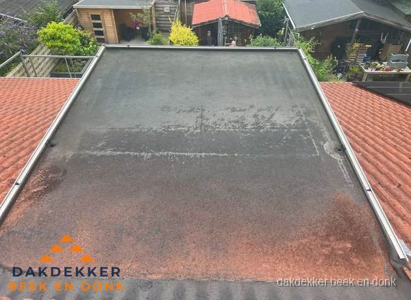 Verouderd plat dak met slijtage tussen schuine daken in Beek en Donk